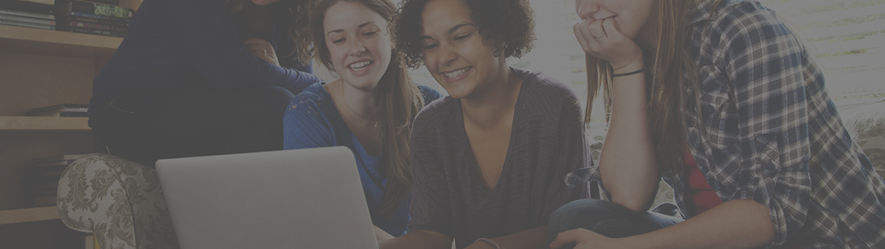 Teen girls sitting on sofa with laptop, laughing